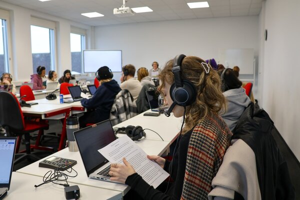 Ein Klassenzimmer voller junger Erwachsener, die alle ein Headset tragen und vor ihrem Laptop sitzen.
