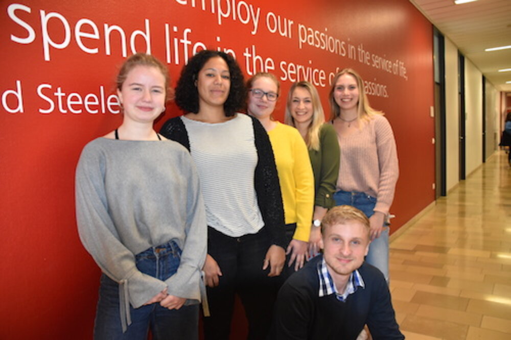 Gruppenfoto vom Helferteam beim Careerday Das Helferteam vom Careerday posiert vor einer roten Wand mit weißem Text in einem Flur.