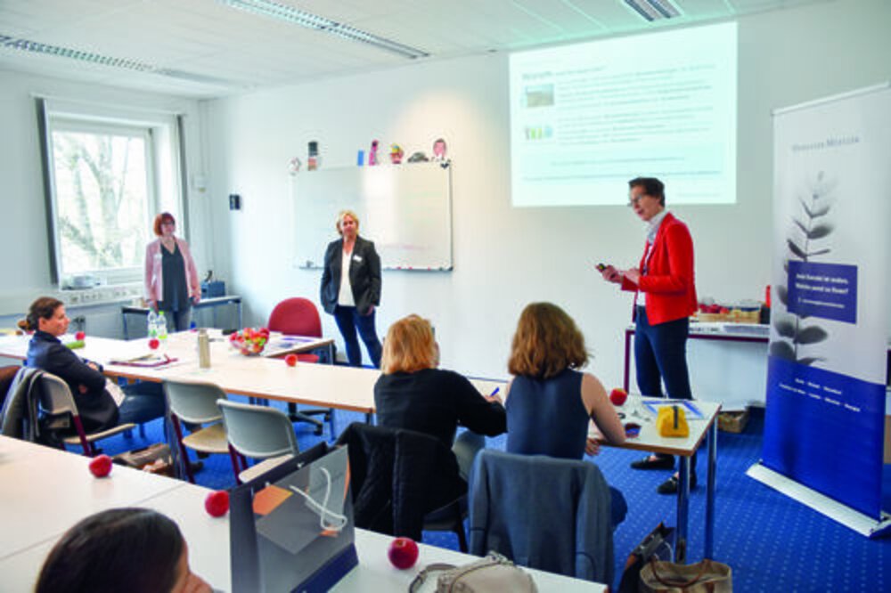 Präsentation in einem Seminarraum Personen in einem Raum verfolgen eine Präsentation vor einer Leinwand; Tische, Whiteboard