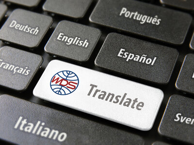 Nahaufnahme einer Computertastatur mit Tasten, die verschiedene Sprachen anzeigen, darunter Deutsch, Englisch, Französisch, Spanisch, Portugiesisch und Italienisch. Eine hervorgehobene weiße Taste mit der Aufschrift „Translate“ und einem WDS-Logo symbolisiert die Übersetzungsfunktion.