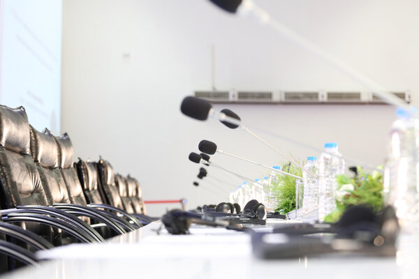 Konferenzraum mit einer Ausstattung für Simultanübersetzungen Eine Reihe von bequemen Stühlen in einem Konferenzraum mit Mikrofonen und Kopfhörern auf einem Tisch, begleitet von Wasserflaschen und kleinen Pflanzen. Der Raum ist hell und scheint auf Simultanübersetzungen vorbereitet worden zu sein.