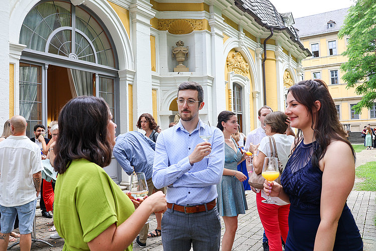 Mehrere Lehrkräfte und Absolventinnen stehen im Garten des Juliusspitals bei Sekt und O-Saften zusammen.