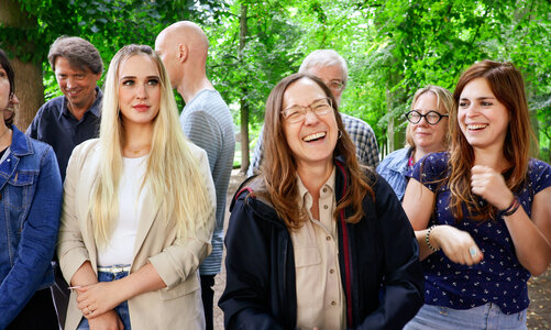 Eine Gruppe lachender Frauen und Männer vor einem Hintergrund aus grünen Bäumen.