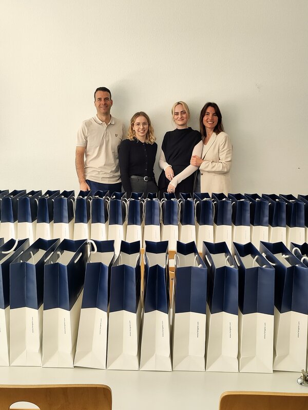 Ein Mann und drei Frauen stehen hinter einem Tisch voller blau-weißer Papiertüten