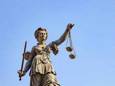 Statue der Justitia mit Schwert und Waage vor blauem Himmel