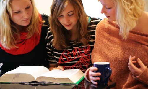Drei Personen sitzen zusammen mit einem offenen Buch auf dem Tisch