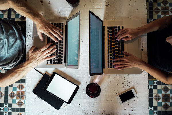 Draufsicht auf zwei Personen am Laptop Zwei Personen arbeiten sich gegenüber sitzend an Laptops an einem Tisch.
