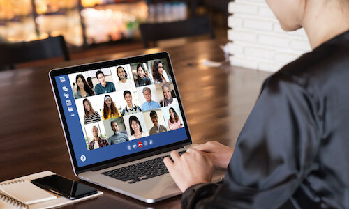 Person bei einem Videoanruf am Laptop, mit Notizbuch und Handy auf dem Tisch