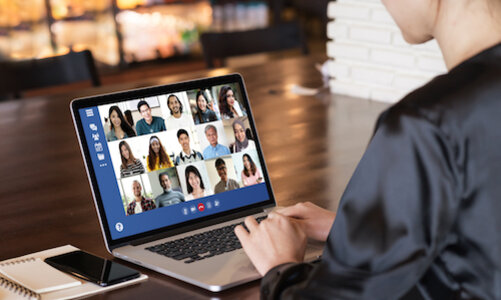 Person bei einem Videoanruf am Laptop, mit Notizbuch und Handy auf dem Tisch