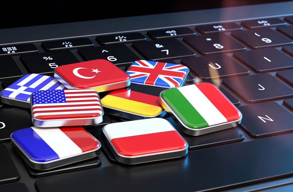 Nahaufnahme einer Laptoptastatur. Darauf liegen einzelne Tasten, die jeweils eine Flagge darstellen: Griechenland, USA, Frankreich, Türkei, Deutschland, Vereinigtes Königreich, Polen und Italien.